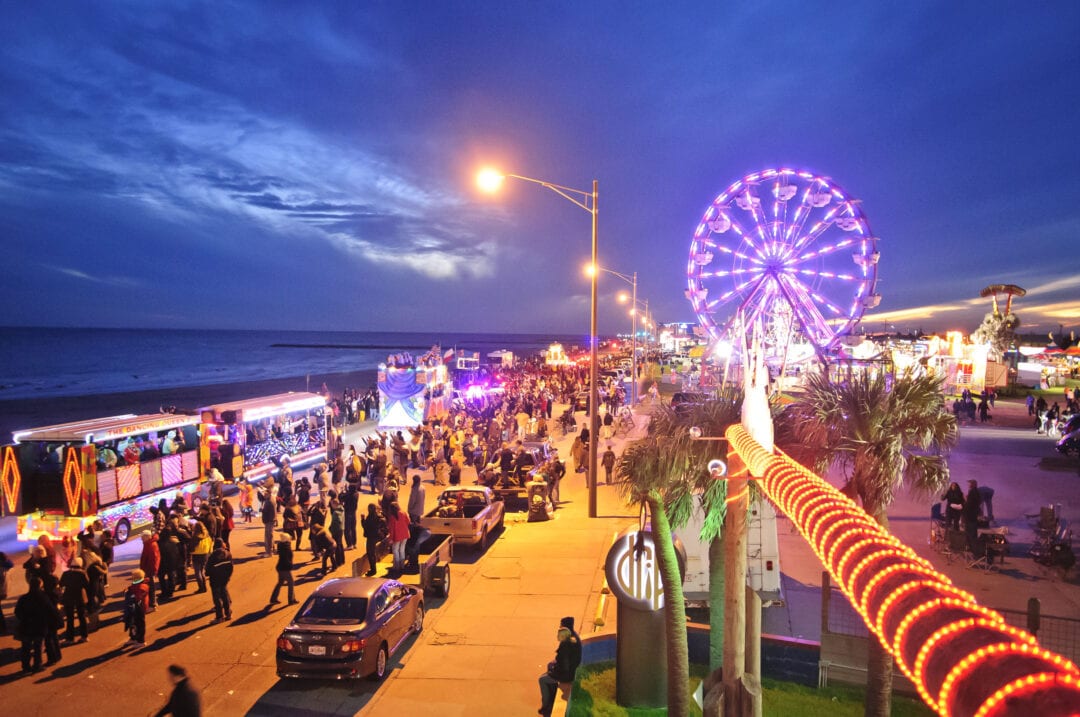 A colorful parade rides along an oceanfront boardwalk in Galveston at nighttime.