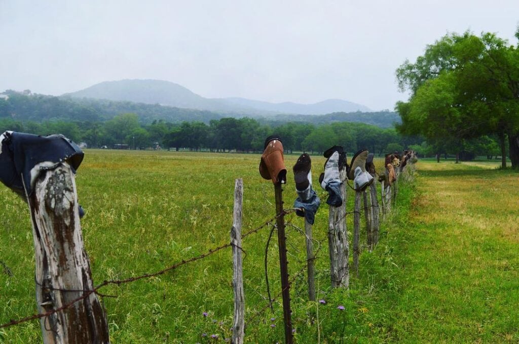 Boots line a rustic fence in a mountainous landscape.