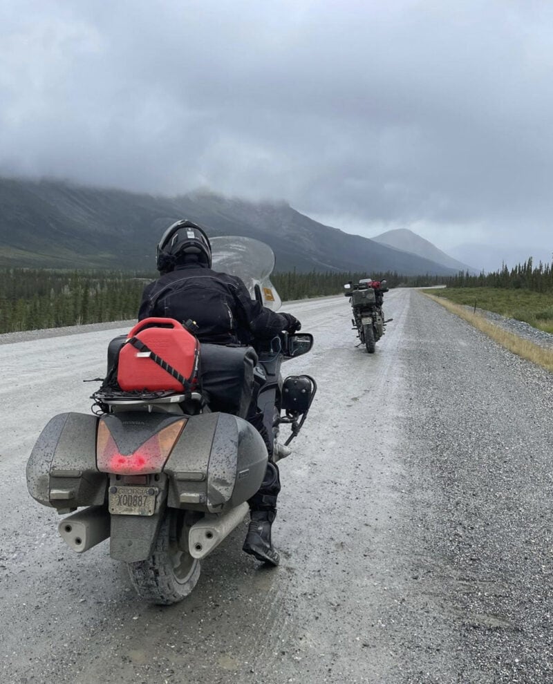 Two motorcycles on a gravel road surrounded by mountains and gray sky