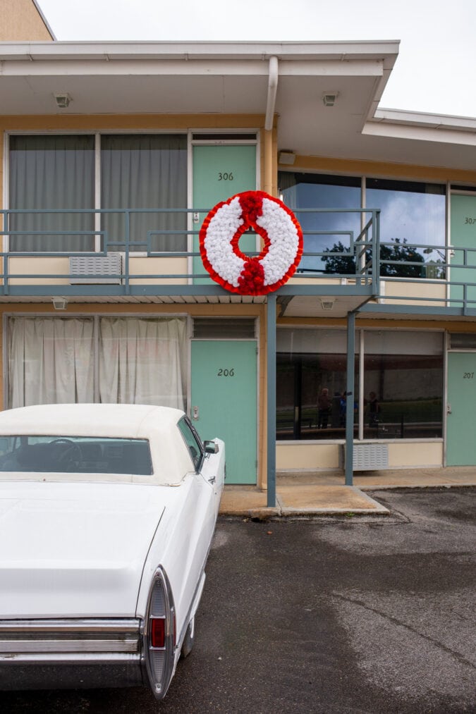 a hotel balcony with a red and white wreath and a vintage car parked below