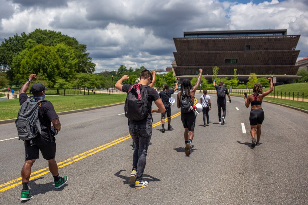 A group of Black Lives Matter marchers walk in the street with their fist held high past the National Museum of African American History and Culture