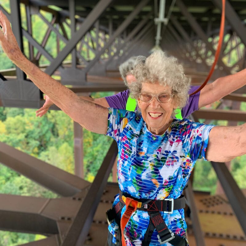 A grandmother extends her arms and looks excited as she tackles a narrow elevated walkway.