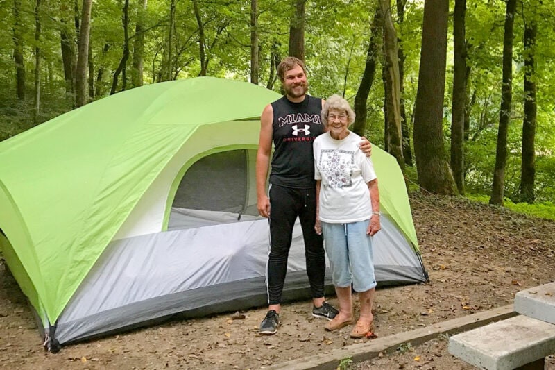 A grandmother and her adult grandson stand in front of a tent.