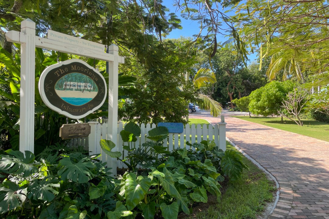 A sign for Moorings Village stands at the entrance to a quaint, tree-lined pathway.