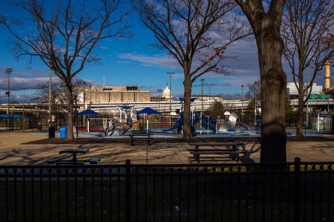 the white dome of the u.s. capitol visible through trees surrounded by a playground and concrete buildings