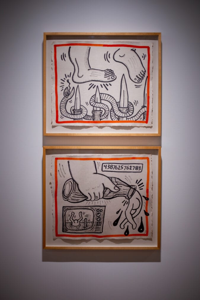 two black and white ink drawings depicting feet and knives and a hand holding a bottle in wooden frames on a white wall