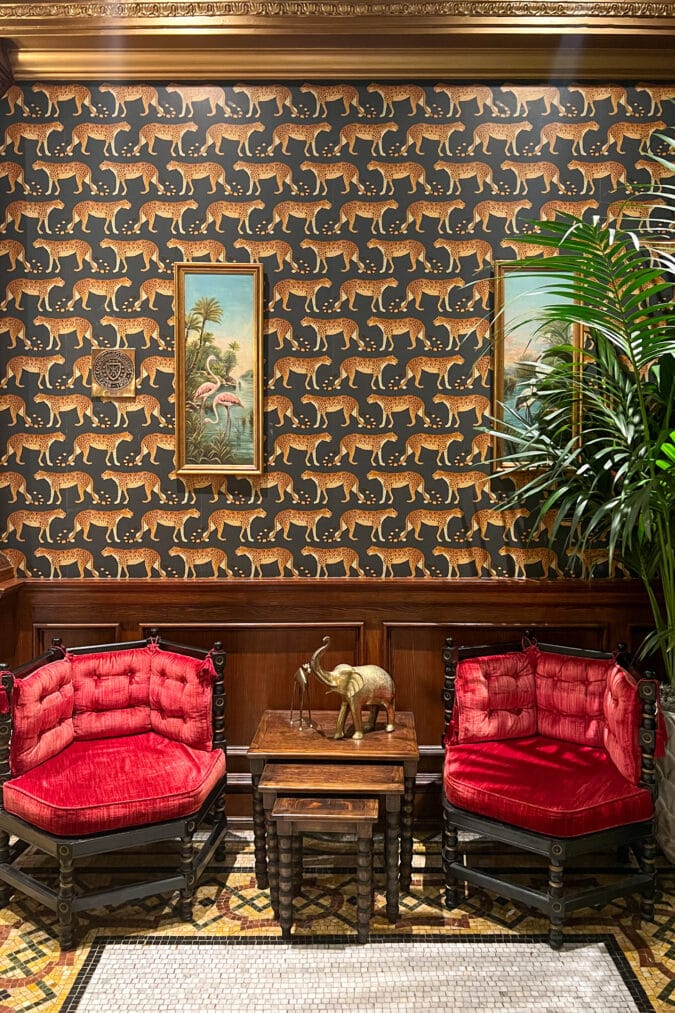 Vivid wallpaper adorns a wall in a room decorated with red velvet chairs.