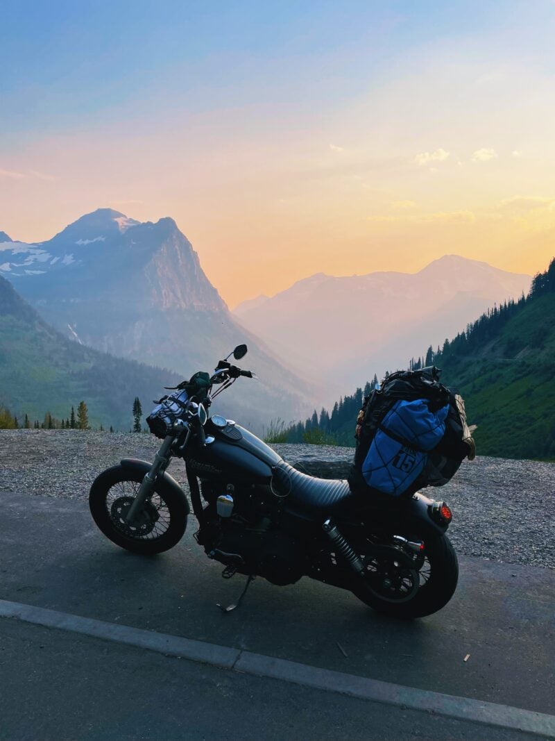 A lone motorcycle is parked on a roadside overlook at Glacier National Park, offering views of purple-hued mountains