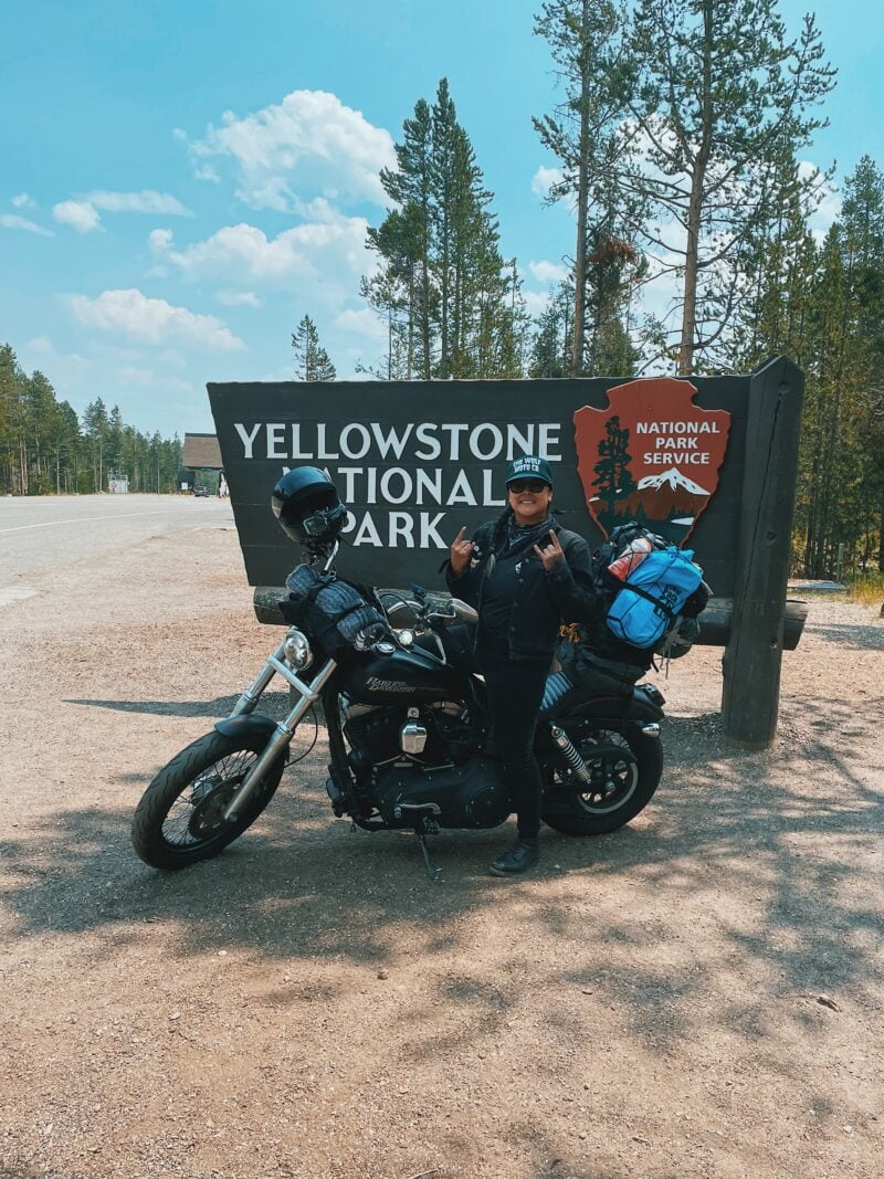 The author sits on her motorcycle in front of the sign for Yellowstone National Park