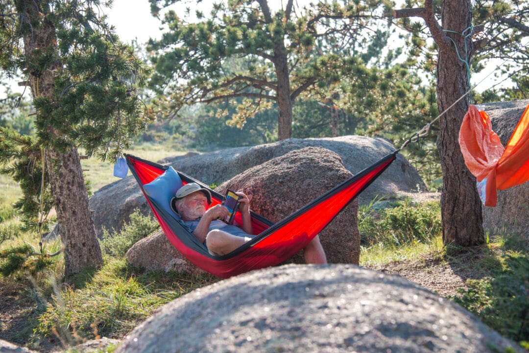 A person reclines in a hammock while reading a book
