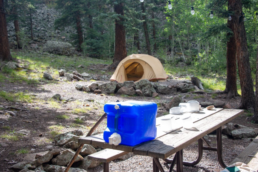 A large blue water jugs sits atop a picnic table at a campsite