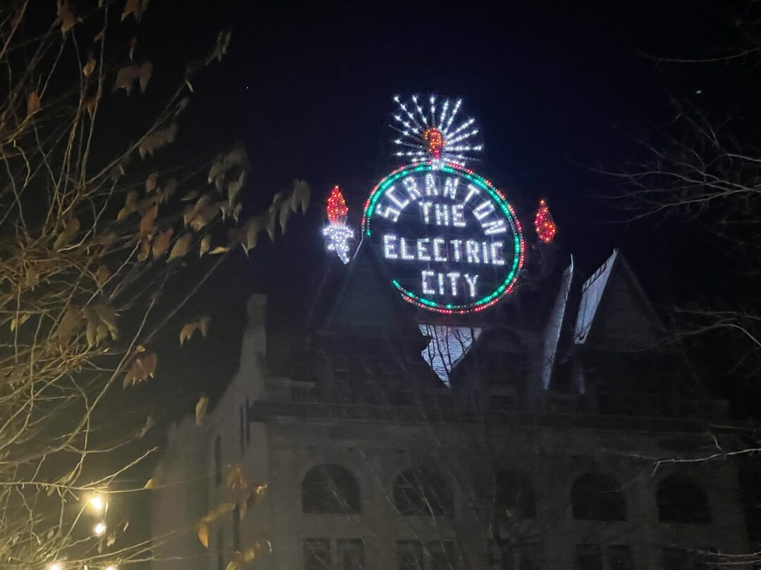 A neon sign is lit up at night, reading "Scranton, The Electric City."