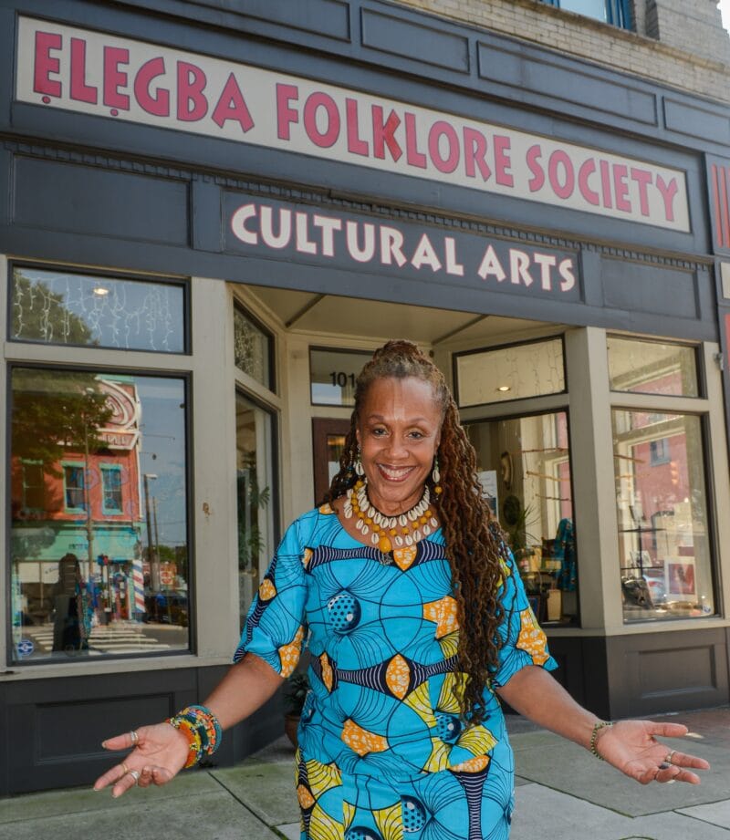 A woman extends her arms as she welcomes visitors into the Elegba Folklore Society building.
