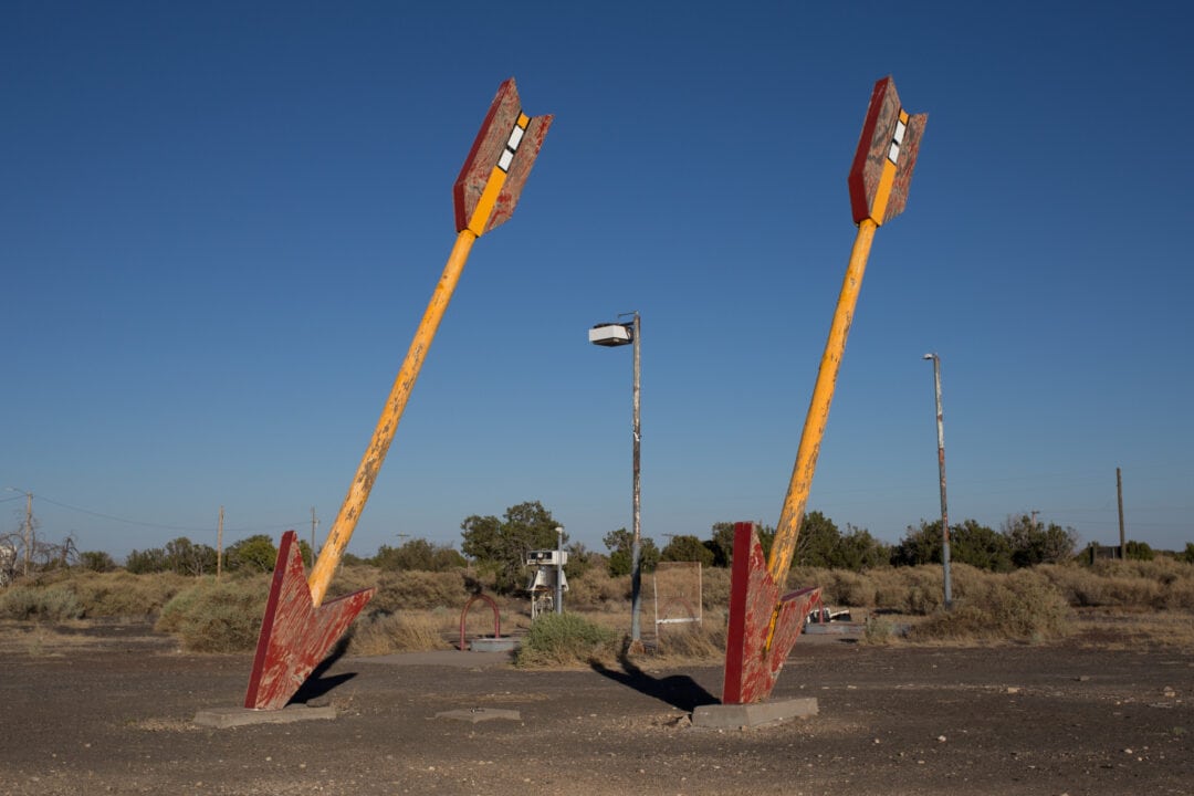 two large wooden arrows painted red and yellow stuck in the ground against a clear blue sky