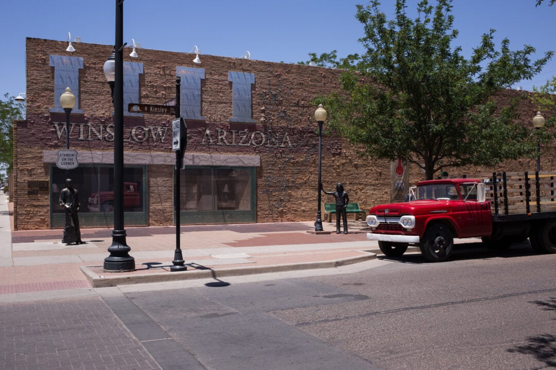 a brick building on a corner with two bronze statues and a red flatbed ford truck parked nearby