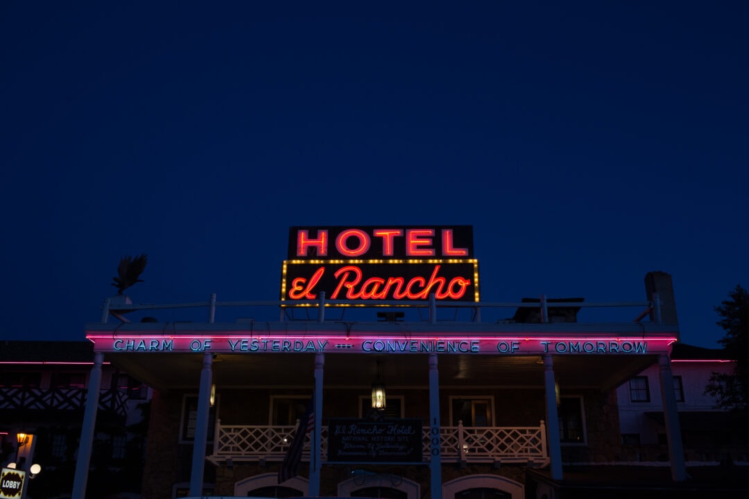 the front of the hotel el rancho at night, with blue, red and pink neon signs lit up against the dark sky