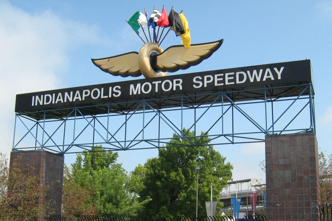 entrance gate to the Indianapolis Motor Speedway with a tire and wings logo and several flags