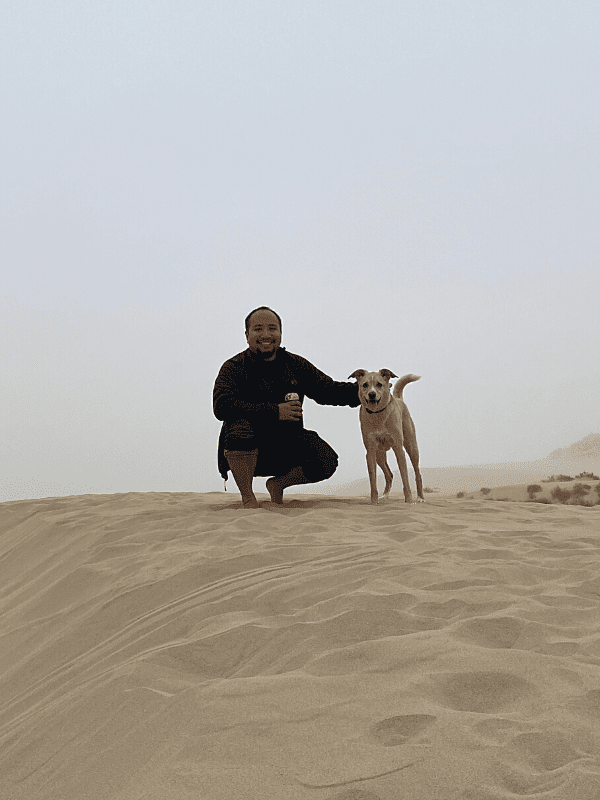 A man and a dog stand atop the sandy Pismo Dunes.
