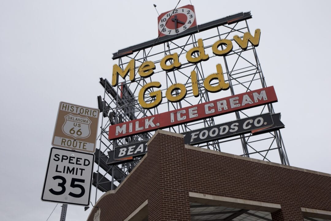 a meadow gold neon sign with a clock on top of a brick building next to a sign for historic route 66 and a speed limit sign for 35 mph