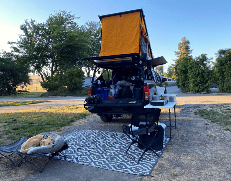 A truck camping setup that includes a pop-up tent and outdoor cooking equipment.