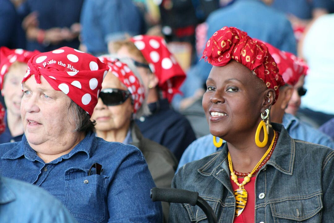 A group on women dress up in homage to Rosie the Riveter, donning her iconic denim coveralls and red head scarf.