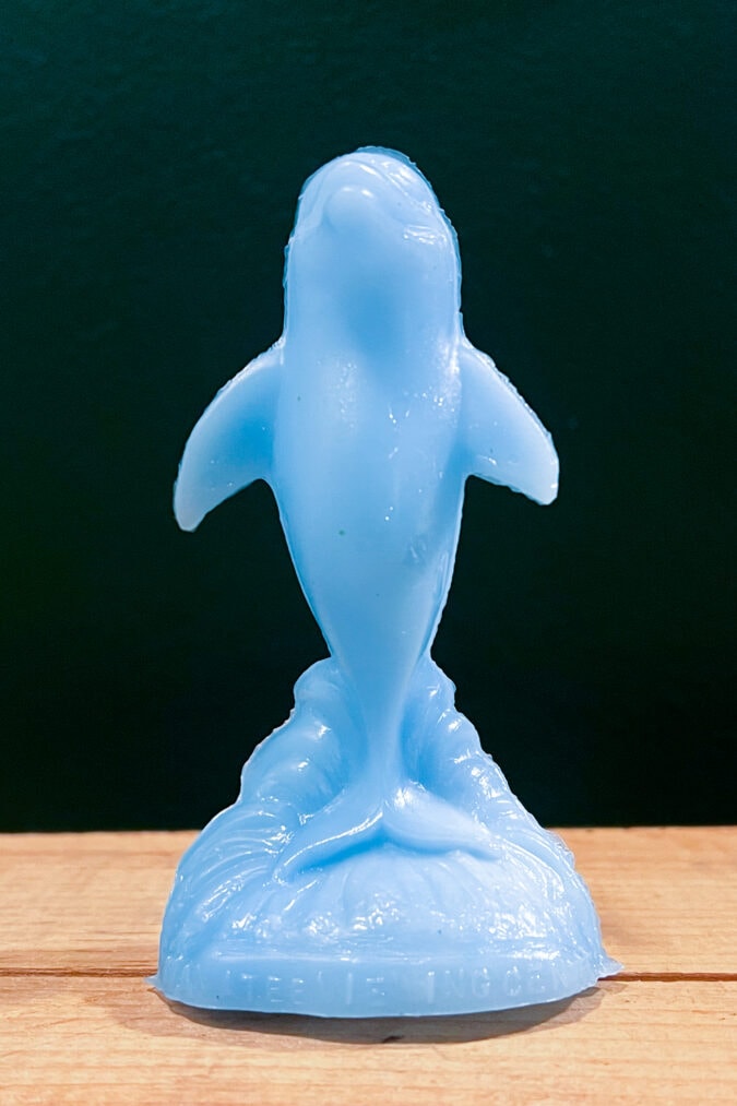 a blue plastic molded dolphin figurine against a dark green background on a wooden crate