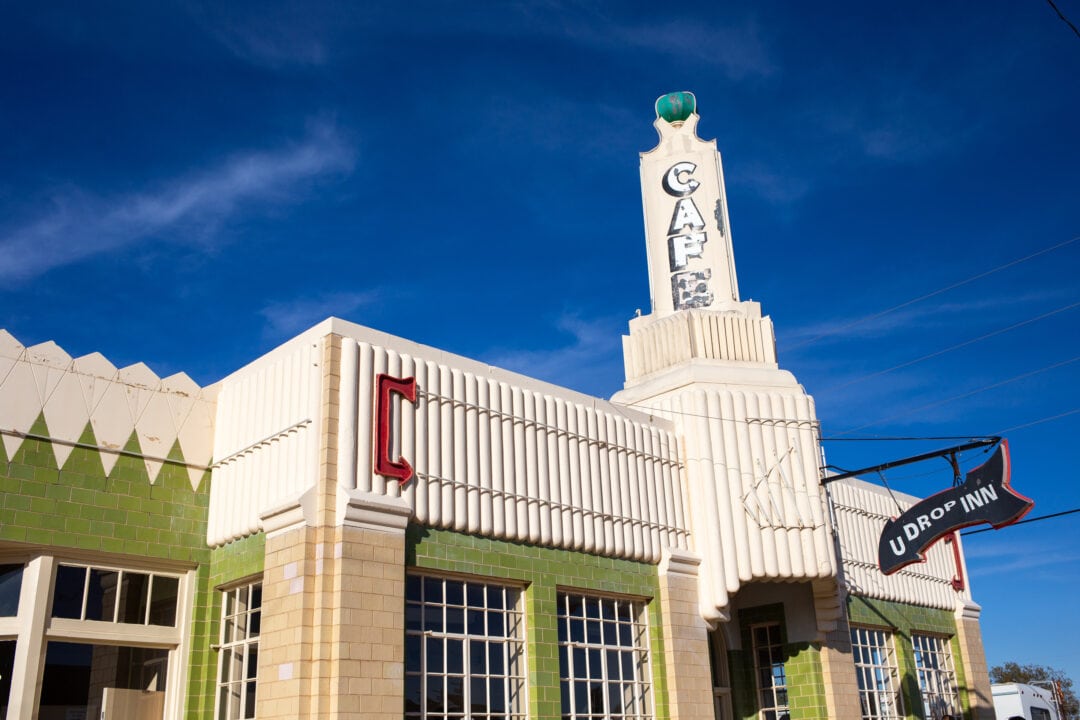 an art deco filling station with a tower that says "cafe" and an arrow sign that says "u drop inn"