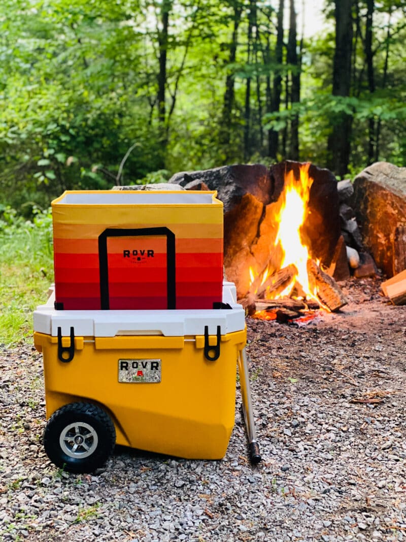 Yellow cooler in front of a campfire with storage box on top