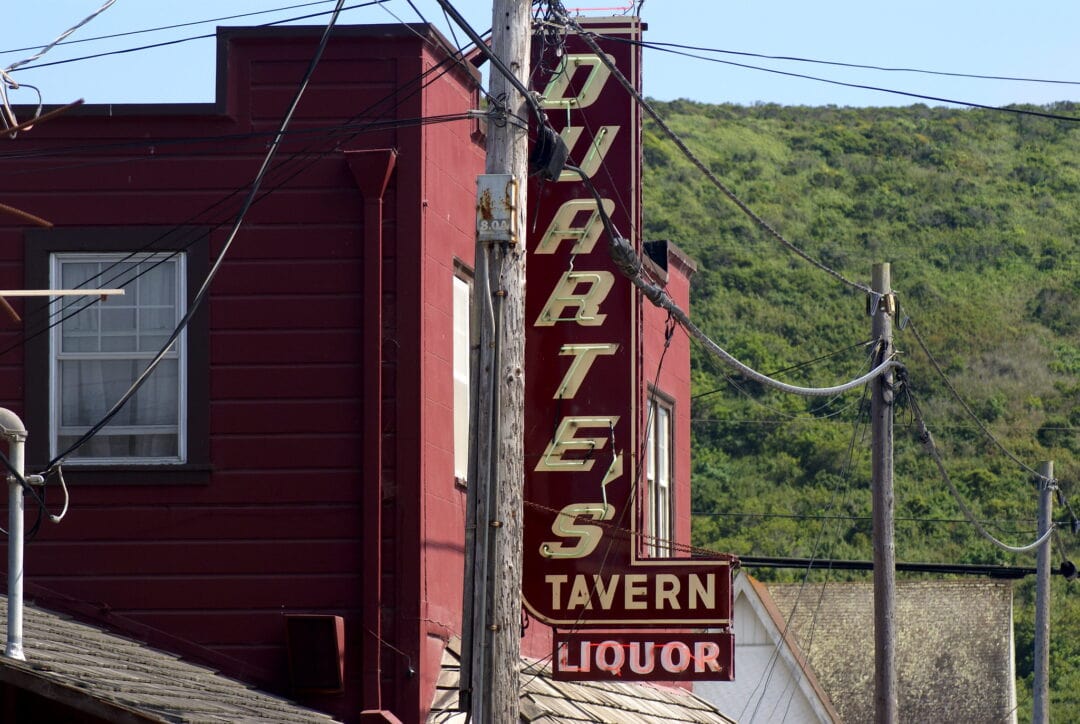 Dark red neon street sign that reads "Duarte's Tavern. Liquor" on side of red brick building.