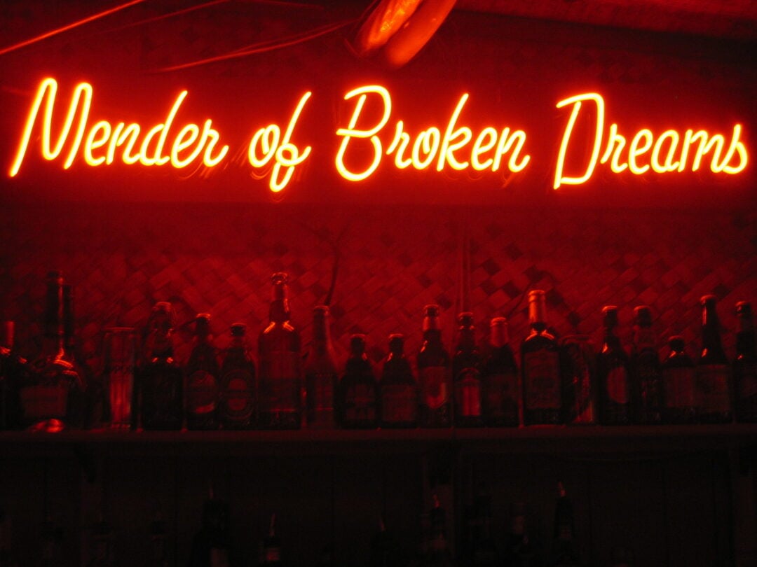 Red neon sign behind dark bar that reads "Mender of Broken Dreams"