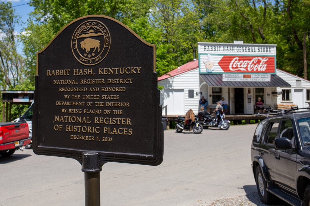 a historical marker for Rabbit hash kentucky stands outside of a general store with motorcycles and cars in the parking lot