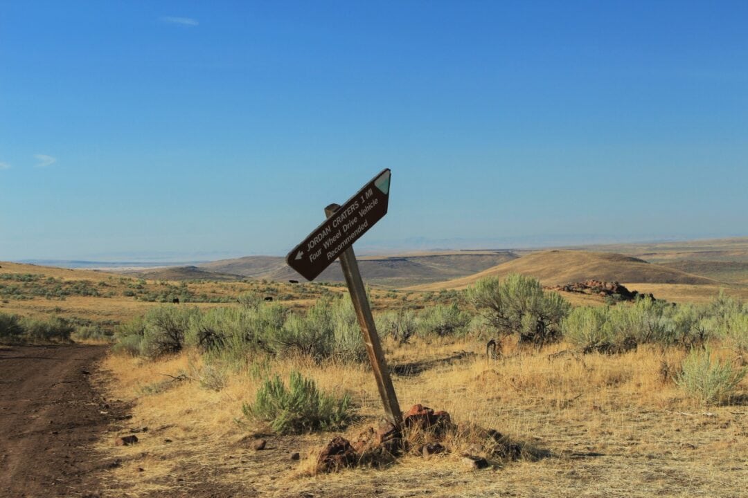 A crooked wooden sign says "Jordan Craters, 1 Mile. Four Wheel Drive Vehicle Recommended."