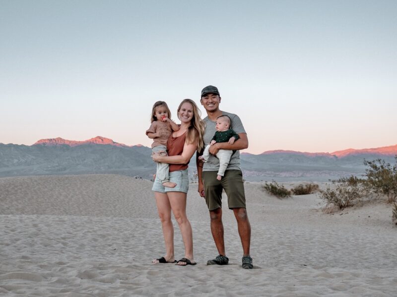 Young family stands in sand dunes at sunset