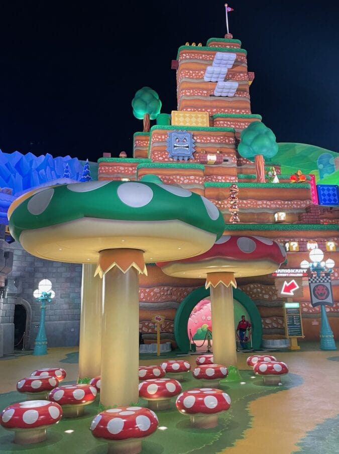 Giant cartoon mushrooms sit in the foreground as a larger-than-life replica of the original Super Mario Bros. gameboard looms in the background