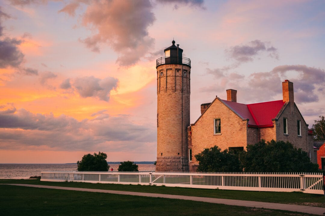 A brick lighthouse abuts the water as a purple sunset illuminates the sky
