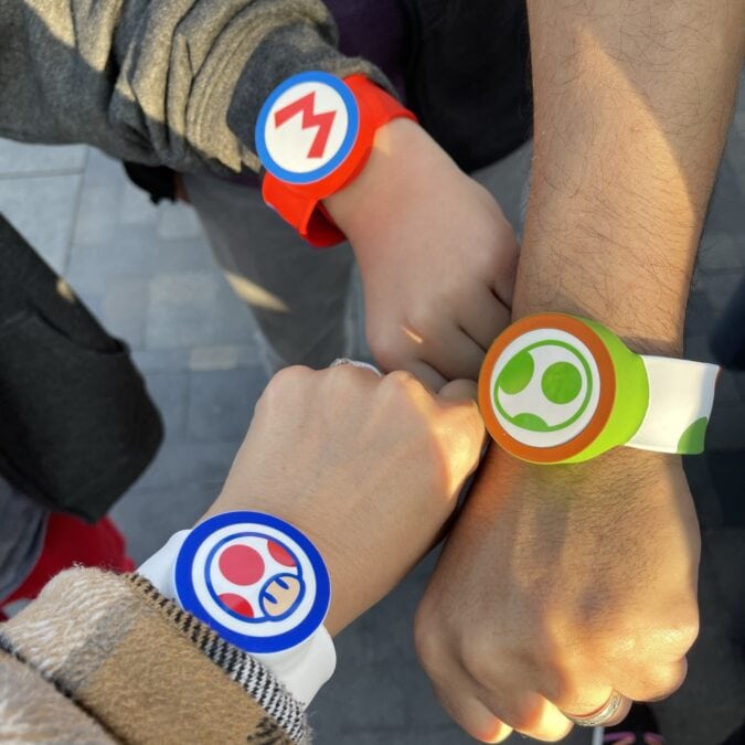 Three people show off themed bracelets featuring designs from the Super Mario video games