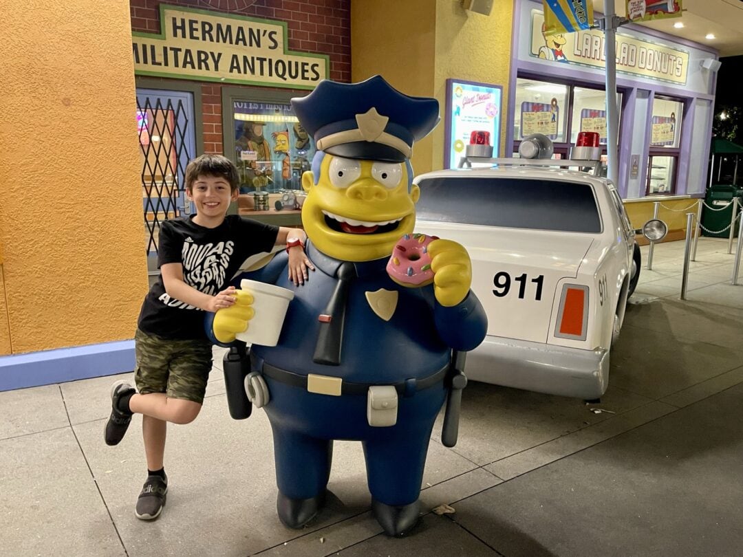 A boy stands next to the police officer from The Simpsons, who is seen snacking on a donut
