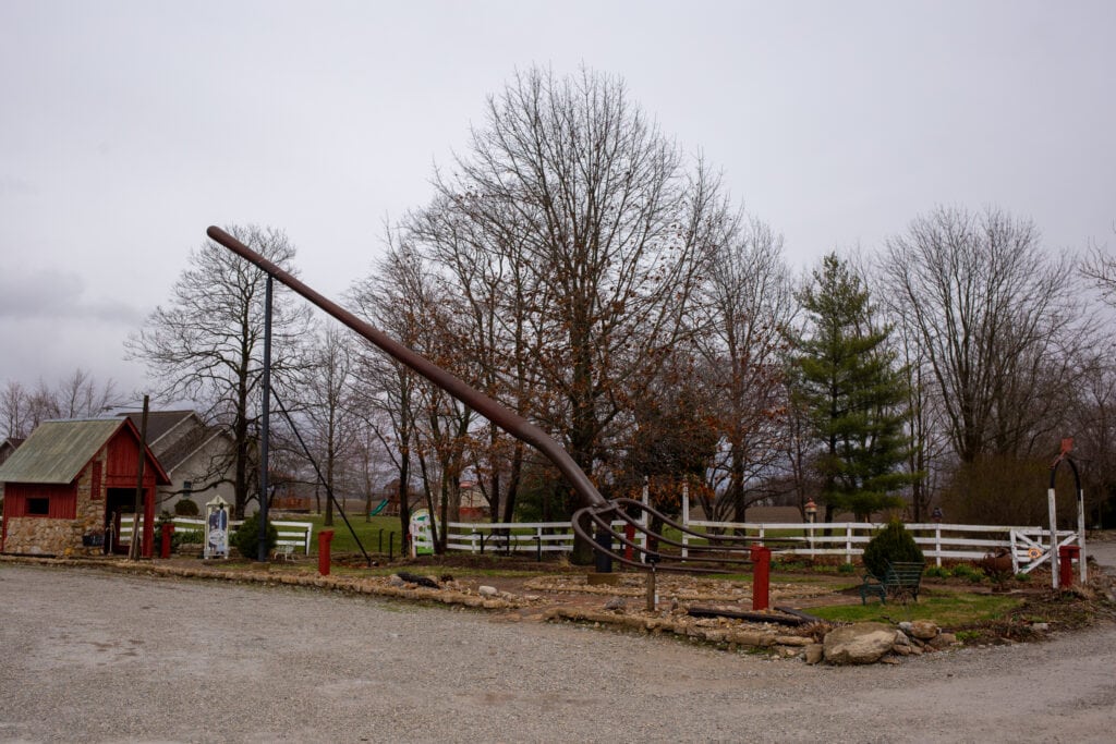 an oversized metal pitchfork sits in the gravel parking lot of a rural restaurant
