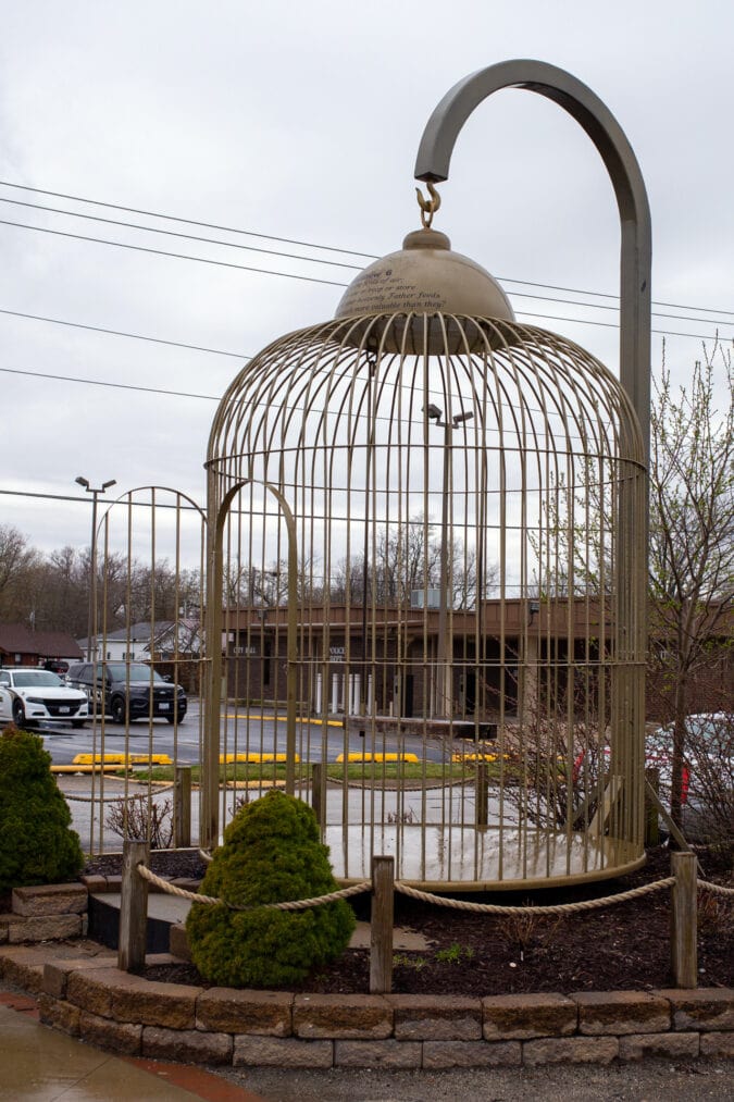 a really large gold birdcage sits on a street corner with its door open