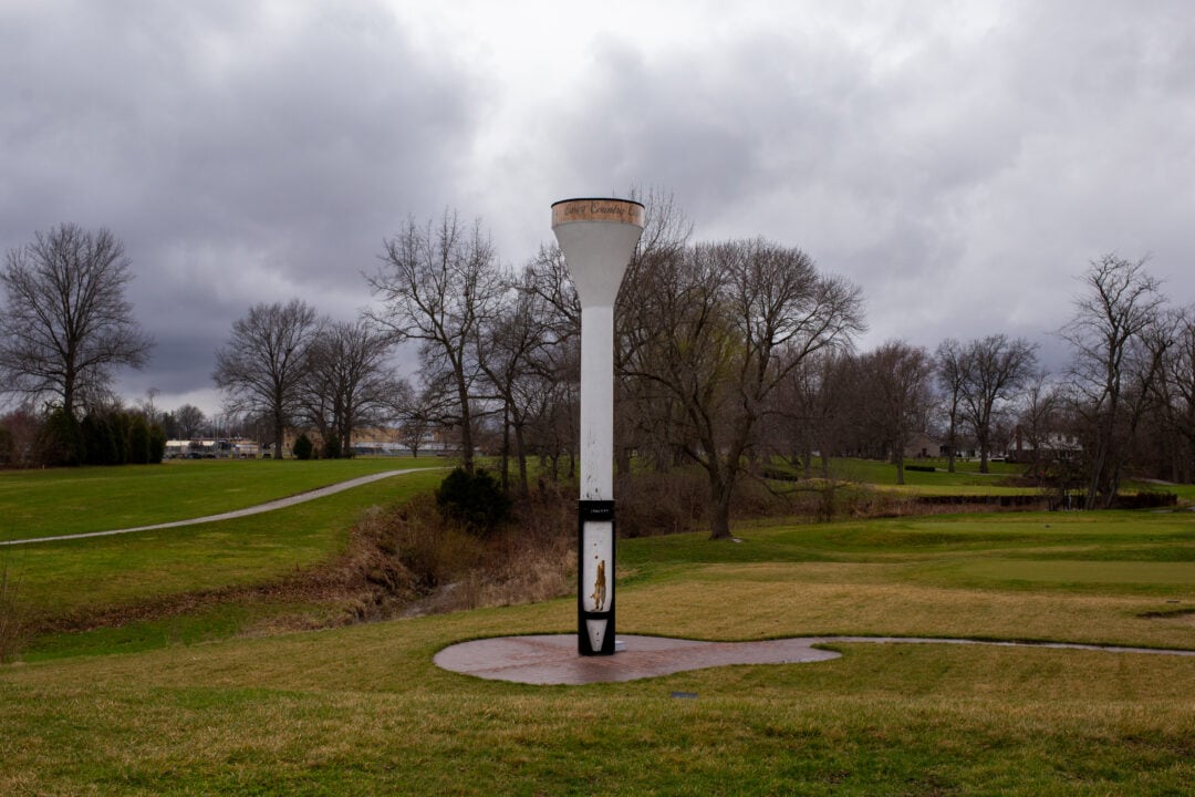 an oversized white wooden golf tee stands in the middle of a green against a cloudy gray sky