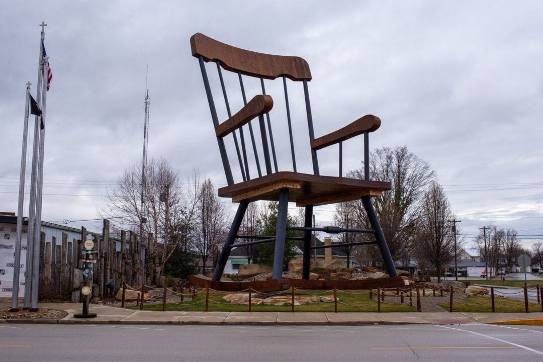 an enormous wooden rocking chair sitting outside against a cloudy gray sky
