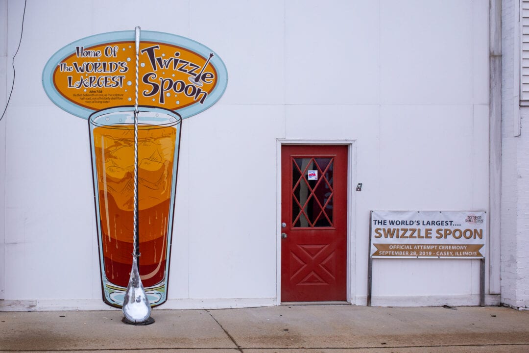 the world's largest swizzle spoon hangs outside of a white building next to a red door