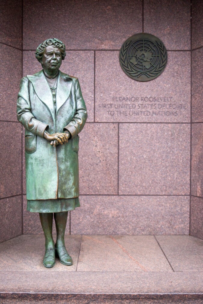 a bronze statue of eleanor roosevelt stands in a granite niche with the emblem for the UN next to her