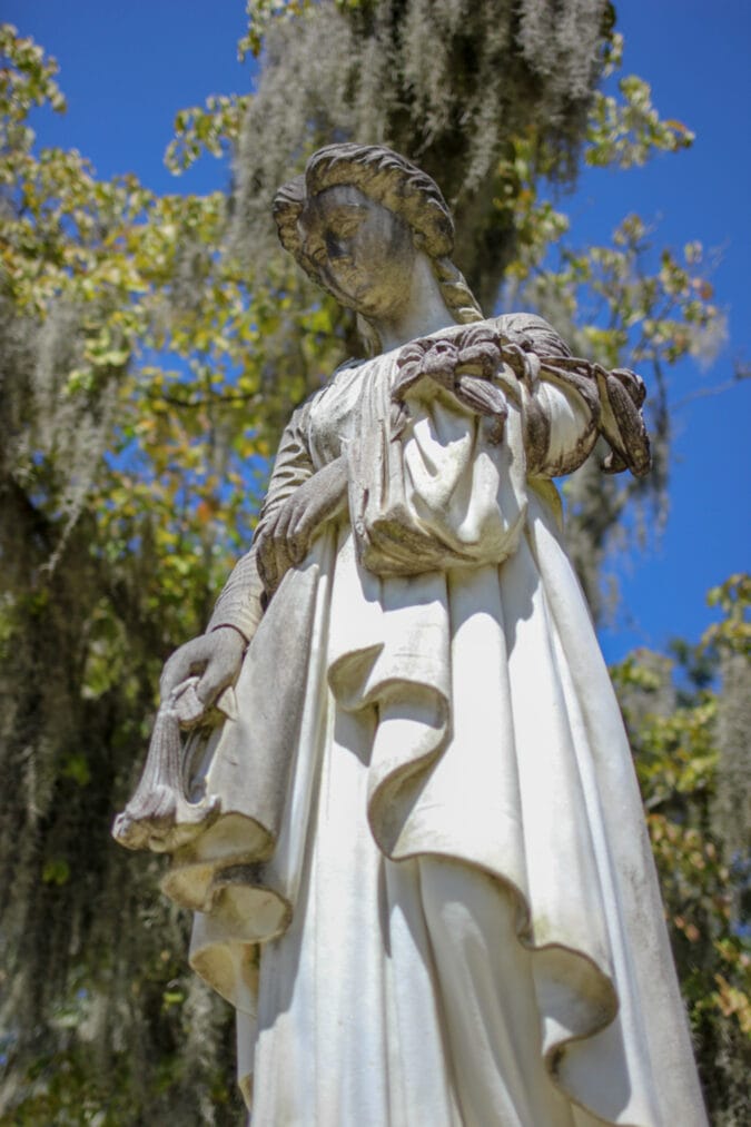 a marble statue of a woman in a cemetery surrounded by spanish moss