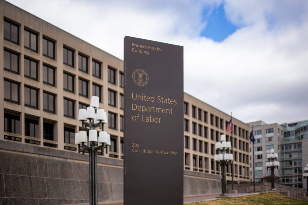 a 6-story concrete brutalist building stretches behind a sign for the frances perkins us department of labor building