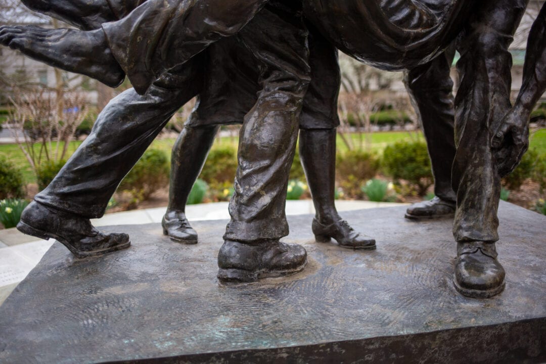 a bronze sculpture of a nurse helping three wounded men with a closeup on their feet