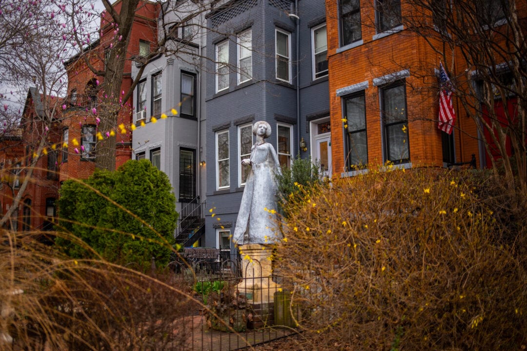 a lead statue of a woman stands outside of a row of colorful brick townhomes