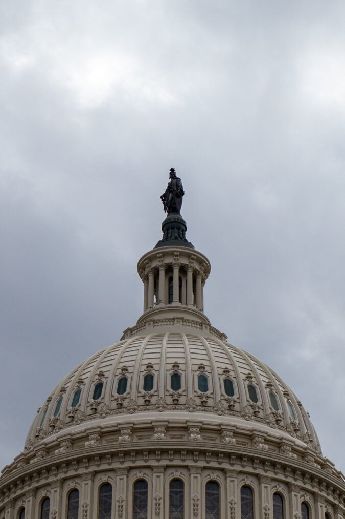 a bronze statue tops the white capitol dome against a cloudy gray sky