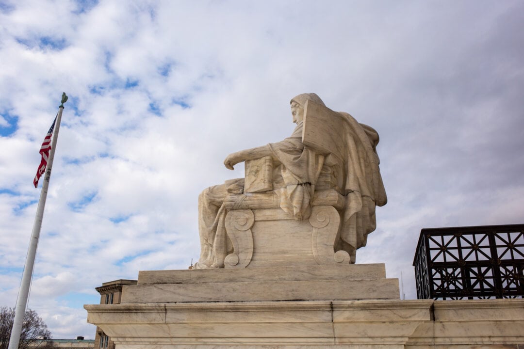 a side view of a stone statue of the contemplation of justice sits at the side of the u.s. supreme court