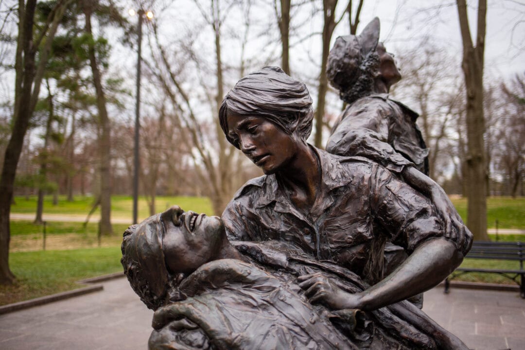 a bronze statue featuring two women nurses helping a fallen soldier